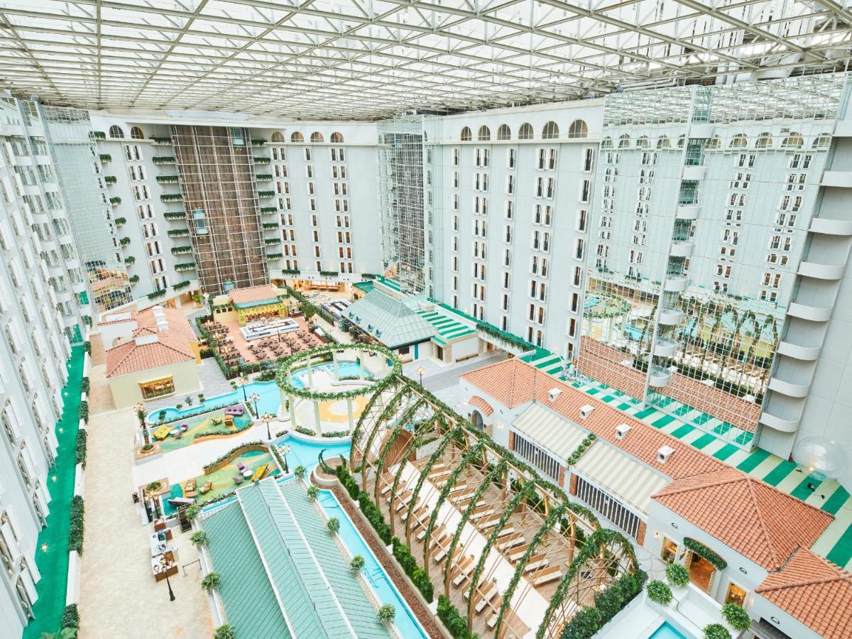 Отель Grand Nikko Tokyo Bay Maihama Ураясу Экстерьер фото The photo shows a large indoor space, likely a hotel or resort atrium. The area features multiple levels of buildings surrounding a central courtyard. This courtyard includes various amenities such as pools, landscaped gardens, and recreational areas
