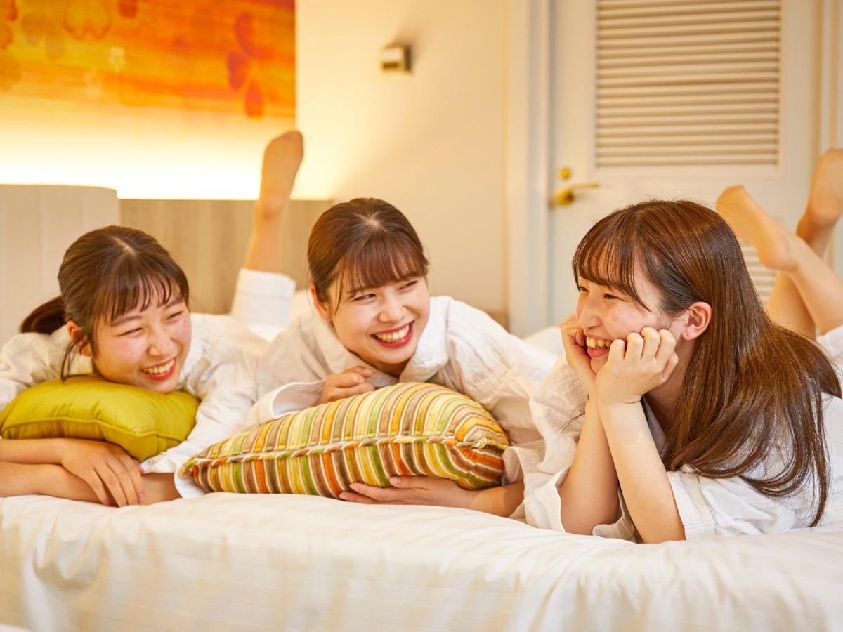 Отель Grand Nikko Tokyo Bay Maihama Ураясу Экстерьер фото The photo shows three young women lounging together in a cozy indoor setting. They are dressed in white robes and appear to be relaxed and enjoying each other's company. The women are lying on a bed, with two of them resting on their arms and the thi