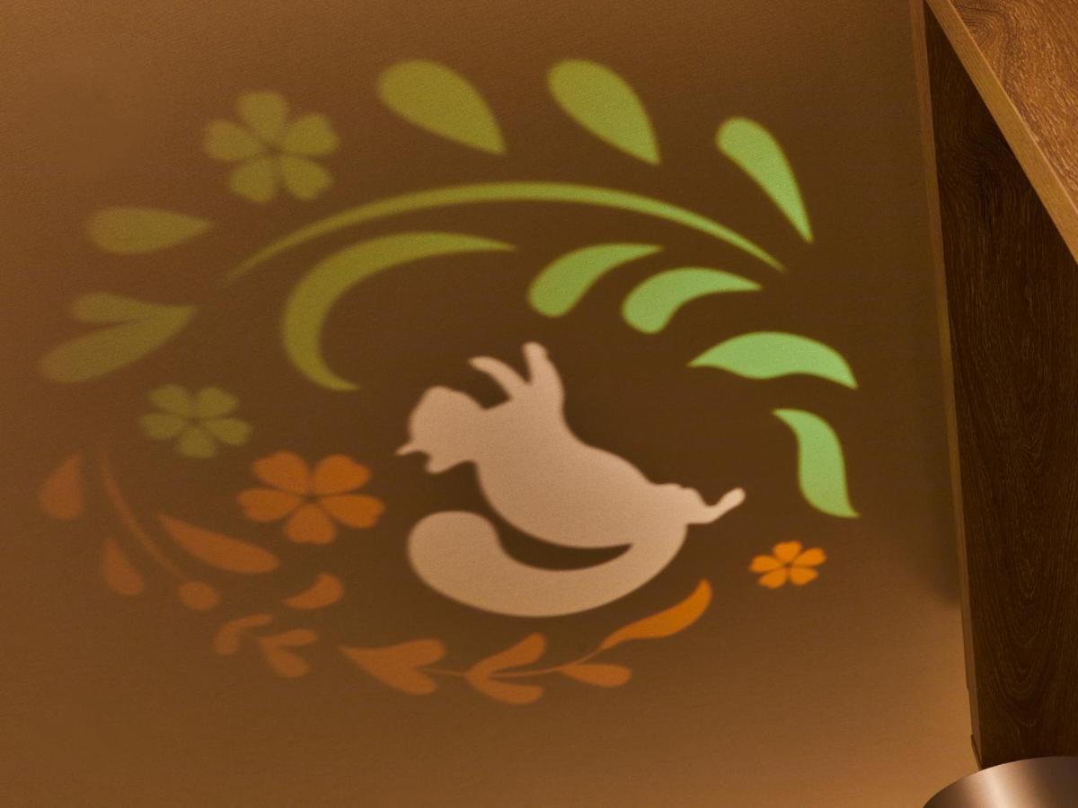 Отель Grand Nikko Tokyo Bay Maihama Ураясу Экстерьер фото The photo shows a colorful projection on a surface that includes a playful illustration. The design features a white silhouette of a squirrel in a lively pose, surrounded by decorative elements like green leaves and flowers in shades of orange and ye