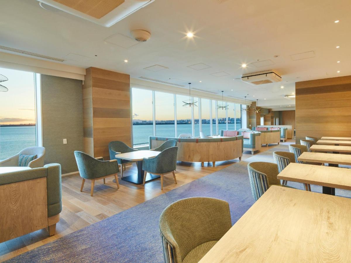 Отель Grand Nikko Tokyo Bay Maihama Ураясу Экстерьер фото The photo shows a modern interior space, likely a dining or lounge area. It features large windows that offer a view of the water, allowing natural light to fill the room. The decor includes wooden walls and stylish, comfortable furniture, with sever