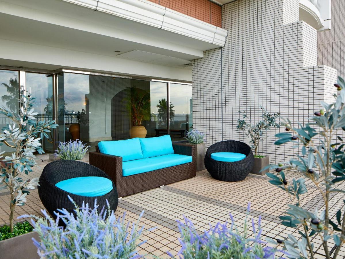 Отель Grand Nikko Tokyo Bay Maihama Ураясу Экстерьер фото The image shows a stylish outdoor seating area. There is a brown couch with turquoise cushions, complemented by two matching round chairs nearby. The seating is arranged on a tiled patio, which is bordered by planters featuring lavender flowers and g