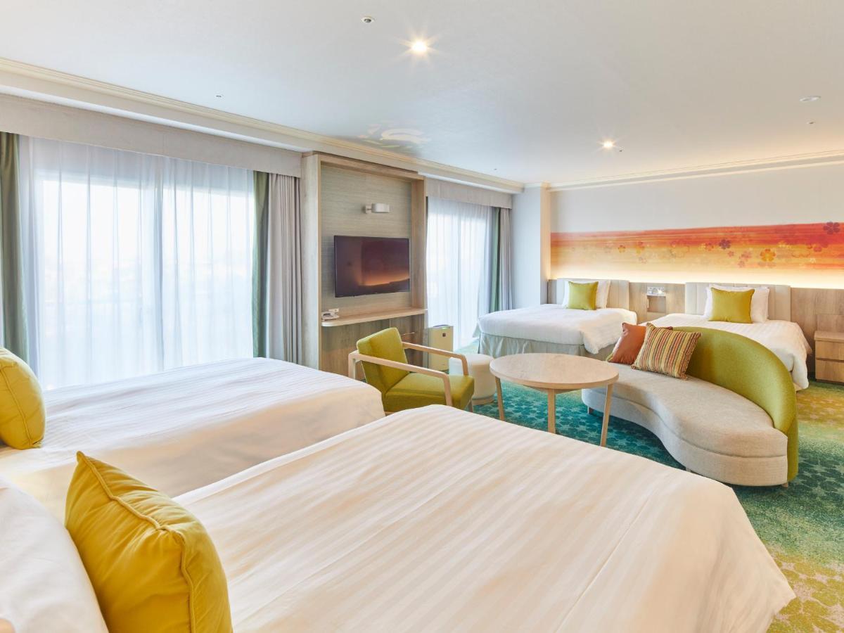 Отель Grand Nikko Tokyo Bay Maihama Ураясу Экстерьер фото The photo shows a modern hotel room that features two large beds covered with white bedding and decorative pillows. There is a contemporary, curved sofa in a light color, along with a round table in the middle. The room has large windows that allow n