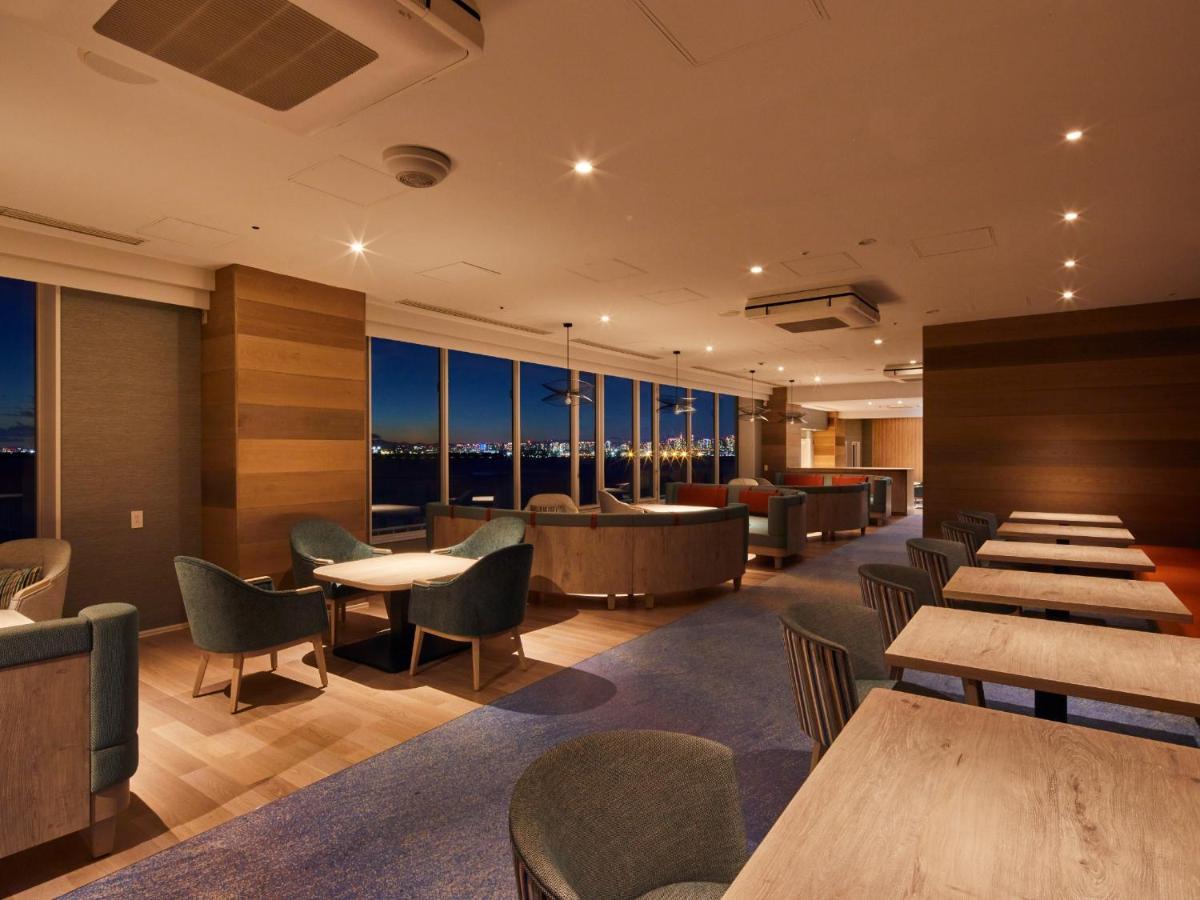 Отель Grand Nikko Tokyo Bay Maihama Ураясу Экстерьер фото The photo shows a modern, well-lit lounge or café area. It features a mix of seating options, including cozy armchairs and tables with chairs. The space has large windows displaying a view, likely of a city or landscape at dusk, given the nighttime a