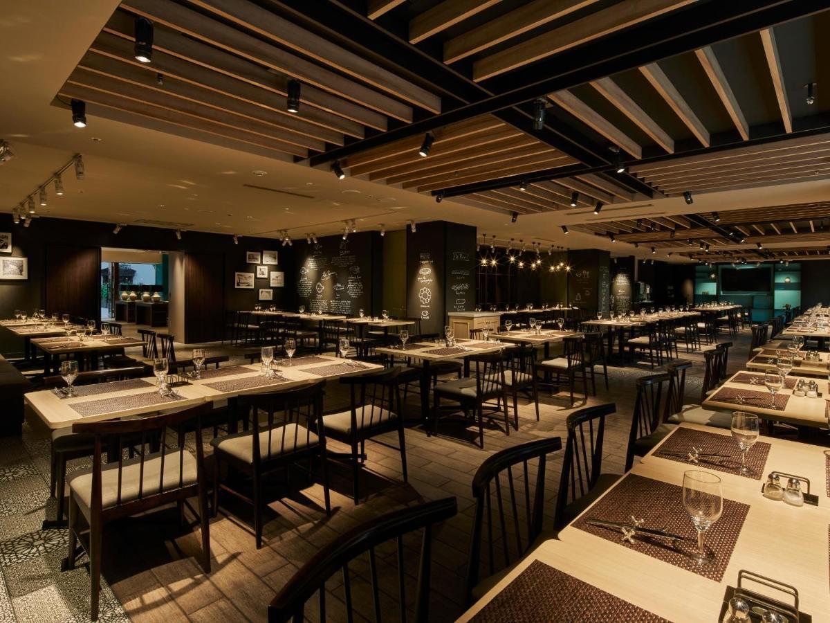 Отель Grand Nikko Tokyo Bay Maihama Ураясу Экстерьер фото The photo shows the interior of a modern restaurant. The space features a spacious dining area with several long tables arranged in rows. Each table is set with dining utensils, plates, and glasses, indicating readiness for patrons. The lighting is s