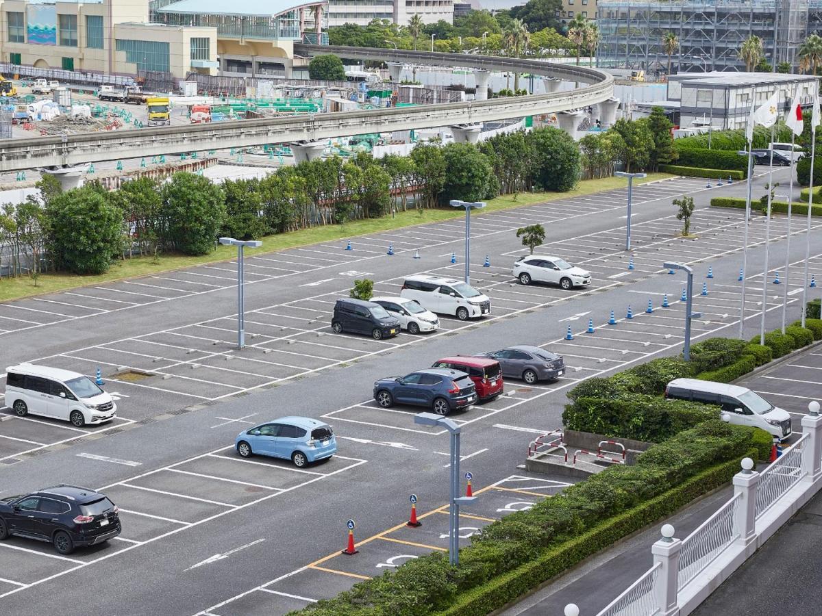 Отель Grand Nikko Tokyo Bay Maihama Ураясу Экстерьер фото The photo shows a partially empty parking lot with several parked cars. In the foreground, there are a few vehicles, including a blue car and a white one. The lot has clearly marked parking spaces, and there are some trees and shrubs along the sides.