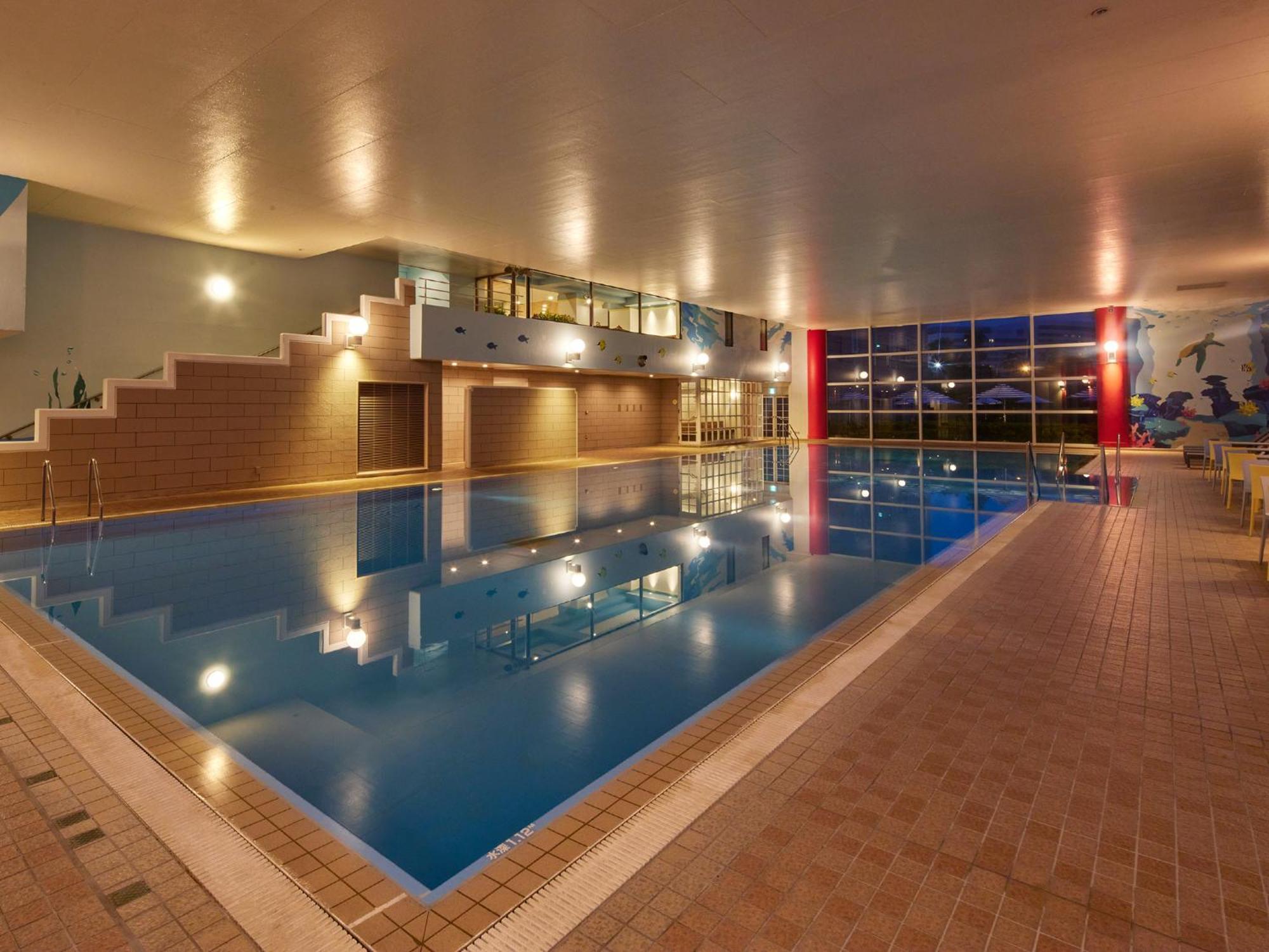 Отель Grand Nikko Tokyo Bay Maihama Ураясу Экстерьер фото The photo shows an indoor swimming pool area. The pool features a calm blue water surface and is surrounded by tiled flooring. There is a staircase leading to a higher level, likely providing access to a lounge or seating area. Large windows allow na
