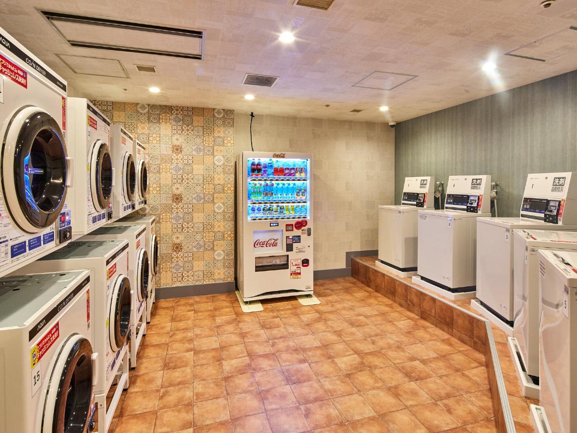 Отель Grand Nikko Tokyo Bay Maihama Ураясу Экстерьер фото The photo shows a laundry room equipped with several washing machines and dryers. On the left side, there are multiple front-loading washing machines arranged in a row, and on the right side, there are dryers. In the center, there is a vending machin